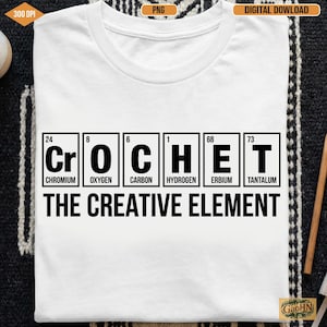 May include: White t-shirt with the word "CROCHET" spelled out using periodic table elements. Below the word is the phrase "THE CREATIVE ELEMENT" in a bold, black font. The shirt is a crew neck style.