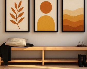 May include: Three framed abstract art prints with black frames hang above a wooden bench. The prints feature botanical and geometric designs in shades of orange and yellow. A pillow and black blanket rest on the bench, with black boots and decorative items.