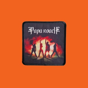 Puede incluir: Parche cuadrado con el nombre de la banda "Papa Roach" en letras góticas blancas. La imagen muestra cuatro figuras silueteadas con los brazos levantados sobre un fondo de humo rojo y naranja. El parche tiene un borde negro.