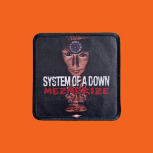 Könnte beinhalten: Quadratischer schwarzer Aufnäher mit dem Bandnamen "SYSTEM OF A DOWN" in Weiß und dem Wort "MEZMERIZE" in Rot. Der Aufnäher hat eine stilisierte Gesichts-Grafik mit einem kreisförmigen Design über dem Kopf.