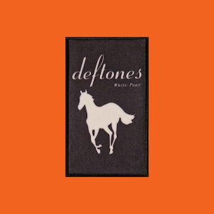 Könnte beinhalten: Schwarzer rechteckiger Aufnäher mit dem Bandnamen "deftones" in weißer Schrift über einer weißen Silhouette eines galoppierenden Pferdes. Die Worte "White Pony" stehen unter dem Bandnamen.