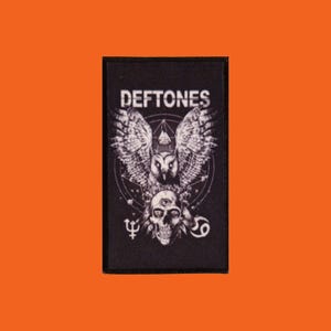 Peut inclure: Écusson rectangulaire noir avec le nom du groupe "Deftones" en haut. Le design présente un hibou aux ailes déployées, un crâne et des symboles astrologiques en gris et blanc. Forme rectangulaire.