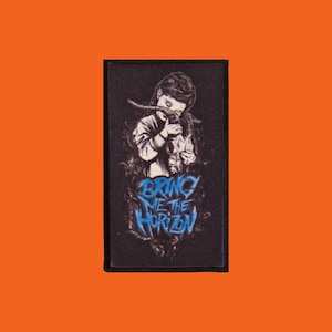 Könnte beinhalten: Schwarzer Aufnäher mit einer detaillierten Illustration einer Person, die einen Schädel mit Hörnern hält. Der Text "BRING ME THE HORIZON" ist in blauer, stilisierter Schrift geschrieben. Der Aufnäher hat einen schwarzen Rand und ist vor einem orangefarbenen Hintergrund platziert.