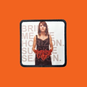Könnte beinhalten: Ein quadratischer Aufnäher mit schwarzem Rand, der eine Frau in einem schwarzen Kleid zeigt, die rote Objekte hält. Die Worte "BRING ME THE HORIZON. SUICIDE SEASON." sind in Weiß auf dem Aufnäher aufgedruckt.