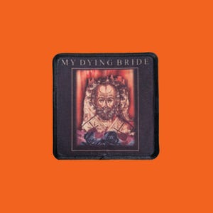 Peut inclure: Écusson carré noir avec une illustration d'un homme barbu avec un halo, sur fond rouge avec des roses. Le texte "MY DYING BRIDE" est en haut de l'écusson.