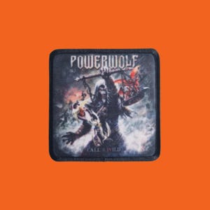 Könnte beinhalten: Ein quadratischer Aufnäher mit dem Text "POWERWOLF" oben und "CALL OF THE WILD" unten. Der Aufnäher zeigt eine dunkle Illustration einer Kapuzenfigur, die eine Waffe hält, mit Flammen und einer wolfsähnlichen Kreatur.