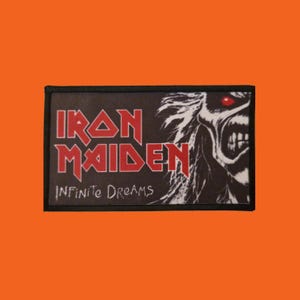 Puede incluir: Parche rectangular negro con el logo de Iron Maiden en rojo y las palabras "Infinite Dreams" debajo. El parche incluye una ilustración detallada de un monstruo con ojos rojos y pelo blanco.