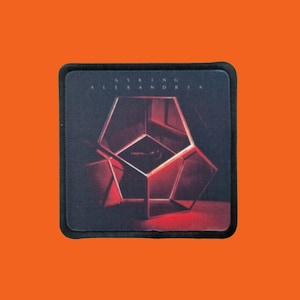May include: Square patch with a black border featuring a geometric design in shades of red and black. The text "ASKING ALEXANDRIA" is printed in white along the top edge of the patch. The patch is set against an orange background.
