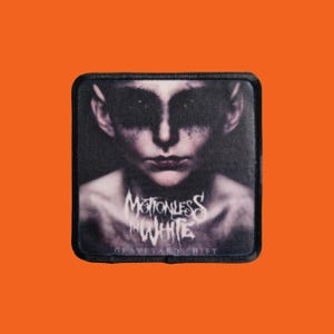 May include: A black square patch featuring a grayscale image of a person's face with dark eye makeup. The text "Motionless in White" is above "Graveyard Shift" in white lettering.