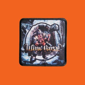 Peut inclure: Écusson carré avec une illustration fantastique d'un guerrier barbu tenant un marteau, sur fond enneigé. L'écusson porte le nom du groupe "Wind Rose" dans une police stylisée, avec une bordure noire.