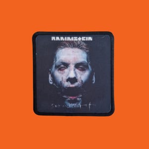May include: Square patch with a black border featuring a portrait of a person with red eyes and the band name "RAMMSTEIN" at the top. The text "Set in sight" is written at the bottom.