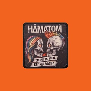 May include: A black square patch featuring two skull illustrations facing each other. One skull has rainbow hair, the other a rainbow mohawk. The word "HÄMATOM" is at the top, with German text below.