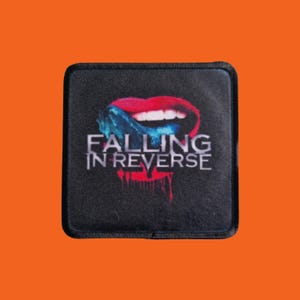 May include: A square black patch with the text "FALLING IN REVERSE" in white, and a graphic of red lips with blue accents. The design includes dripping red paint. The patch has a black border.