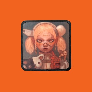 Pode incluir: Remendo quadrado com uma ilustração detalhada de uma menina com tranças loiras, usando fones de ouvido e segurando um brinquedo de pelúcia. O remendo tem uma borda preta e está sobre um fundo laranja.