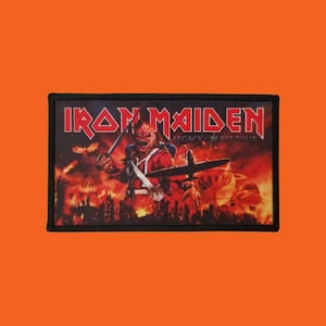 Könnte beinhalten: Rechteckiger Aufnäher mit dem Iron Maiden-Logo in Rot. Das Bild zeigt einen Krieger mit Schwert, Flugzeug und Flammen, mit dem Text "LEGACY BEAST TOUR". Der Aufnäher hat einen schwarzen Rand und ist zum Aufnähen geeignet.