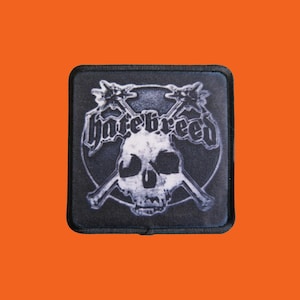 May include: Square patch with a black border featuring a white skull with crossed bones and two spiked clubs. The word "hatebreed" is written above the skull in a gothic font. The background is a dark gray circle.
