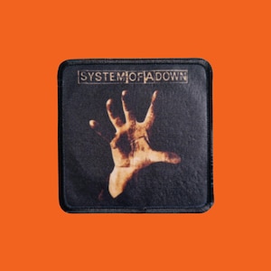 Könnte beinhalten: Ein quadratischer schwarzer Aufnäher mit einer ausgestreckten Hand. Der Bandname "SYSTEM OF A DOWN" ist in einem weißen Rechteck oben aufgedruckt. Der Aufnäher hat einen schwarzen Rand, vor einem orangefarbenen Hintergrund.