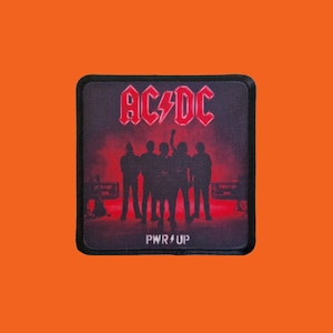 Könnte beinhalten: Quadratischer Aufnäher mit der Band AC/DC und dem Bandlogo in Rot. Der Aufnäher zeigt die Silhouette der Band vor rotem Hintergrund mit dem Text "PWR UP" darunter.