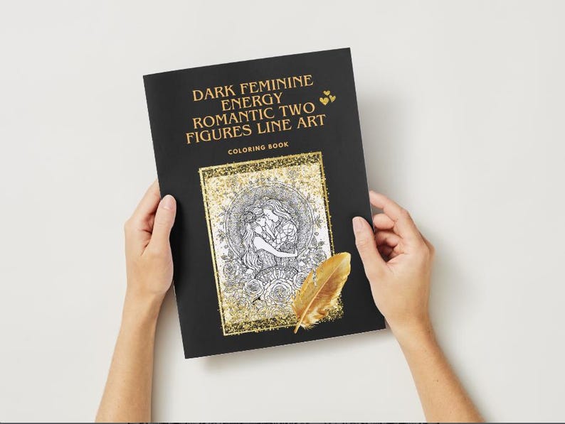 May include: A black coloring book titled "Dark Feminine Energy Romantic Two Figures Line Art" with a gold-framed illustration of two figures embracing. A gold feather rests on the book. The book is held by two hands against a white background.