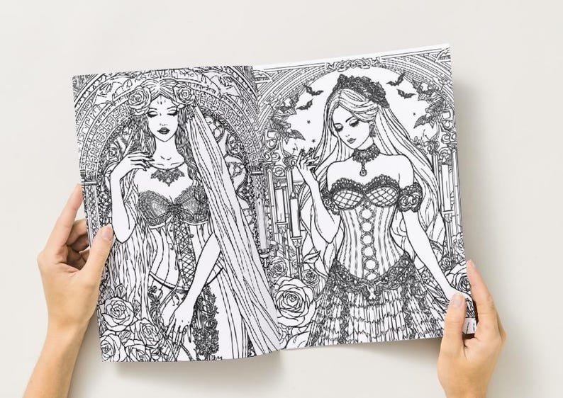 Puede incluir: Una p&aacute;gina doble de un libro para colorear en blanco y negro con dos ilustraciones de mujeres g&oacute;ticas con vestidos elaborados. Los dibujos est&aacute;n detallados con elementos florales y arquitect&oacute;nicos. El libro est&aacute; abierto por manos.