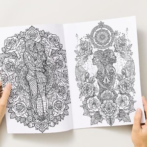 May include: Open coloring book with two detailed black and white illustrations. One depicts a couple embracing within a rose-filled circle. The other shows two faces and a skull surrounded by roses and a mandala.