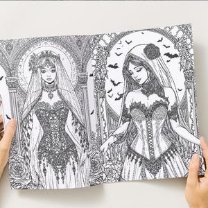 Puede incluir: Una p&aacute;gina doble de un libro para colorear en blanco y negro con dos ilustraciones g&oacute;ticas de mujeres con elaborados vestidos y velos. Los dibujos incluyen elementos florales y arquitect&oacute;nicos detallados, con murci&eacute;lagos en el fondo. El libro est&aacute; abierto por manos.