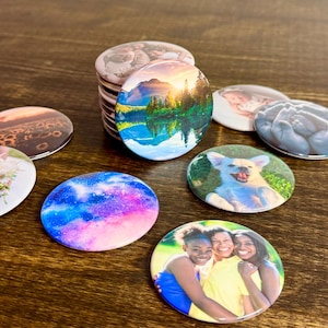 Könnte beinhalten: Eine Sammlung runder Ansteckbuttons mit verschiedenen aufgedruckten Bildern, darunter eine Berglandschaft, ein Galaxiemuster, ein lächelnder Hund, eine Gruppe von drei Personen, ein Blumenfeld und Nahaufnahmen von Säuglingen.