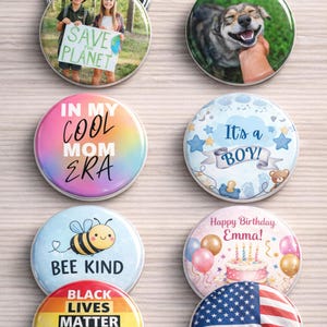 Collection of various buttons with different designs on a wooden surface. Words at the top say "Perfect for all occasions!" One button features children holding a "Save the Planet" sign. Other buttons have text like "In My Cool Mom Era," "It's a Boy!," "Bee Kind," and "Black Lives Matter."