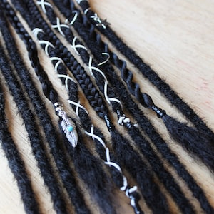 May include: A set of black synthetic dreadlocks with various embellishments, including white string, beads, and a silver feather charm.