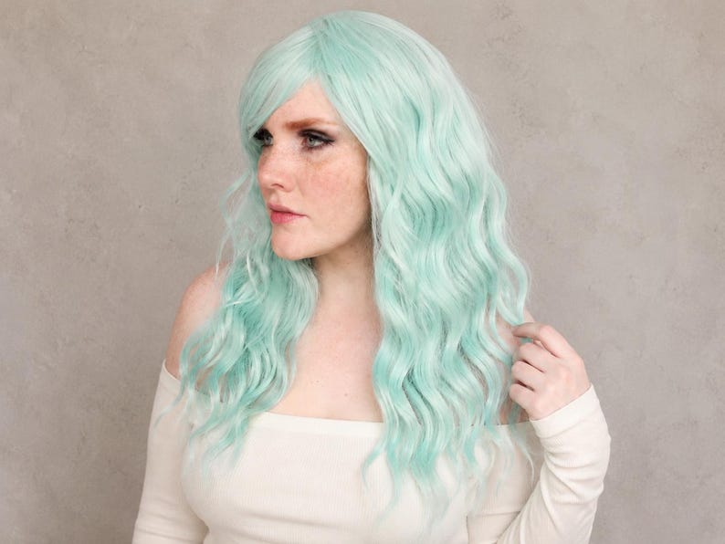 K&ouml;nnte beinhalten: Eine lange, gewellte Per&uuml;cke in blassem Mintgr&uuml;n. Die Per&uuml;cke hat einen seitlich gescheitelten Pony und lockere, flie&szlig;ende Wellen, die &uuml;ber die Schultern fallen. Das Haar hat eine weiche, matte Textur und einen gleichm&auml;&szlig;igen Farbton.