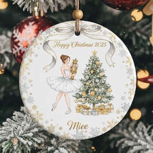 May include: A circular Christmas ornament featuring a ballerina holding a nutcracker, a Christmas tree, and the text "Happy Christmas 2025" and "Miee". The ornament has a ribbon design and gold snowflake accents.