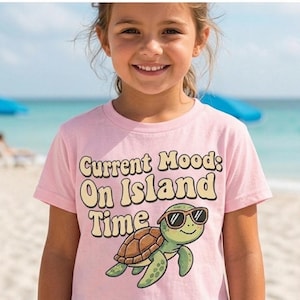 Puede incluir: Una camiseta rosa claro con el texto "Current Mood: On Island Time" y una tortuga de dibujos animados con gafas de sol. La tortuga tiene un caparazón marrón y aletas verdes. El fondo muestra una playa y el océano.