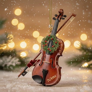 Puede incluir: Adorno de violín en miniatura con arco, una pequeña corona y el año 2025 grabado en el arco. El violín es marrón con una cuerda dorada y un cordón dorado para colgar. La palabra "Name" está grabada en el violín.