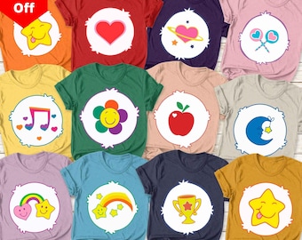 Może przedstawiać: Kolekcja kolorowych koszulek z wzorami Care Bears. Każda koszulka przedstawia inny symbol Care Bears, w tym serce, kwiat i gwiazdę. Koszulki są w różnych kolorach, takich jak czerwony, zielony i niebieski, z logo Care Bears na górze.