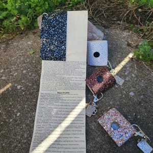 May include: Glittery lighter cases in blue, brown, and pink, with silver keychains. A list of Major Arcana tarot card meanings is visible. The items are displayed outdoors.
