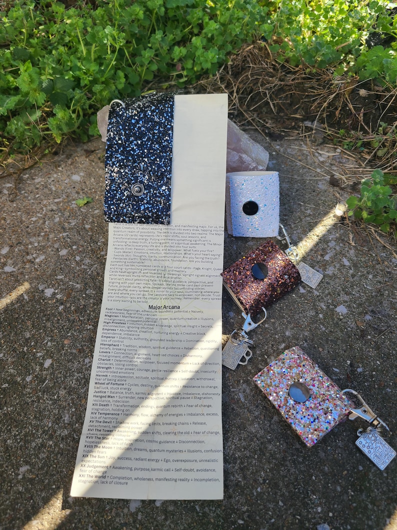 May include: Glittery lighter cases in blue, brown, and pink, with silver keychains. A list of Major Arcana tarot card meanings is visible. The items are displayed outdoors.