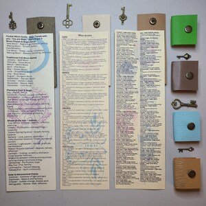 May include: A collection of handcrafted items, including small leather pouches with snap closures, decorative keys, and printed cards with text about moon phases, magic, and tarot card meanings. The items are arranged on a neutral surface.