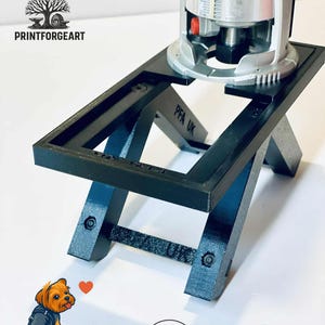Op de afbeelding: Zwarte 3D-geprinte freestafel met een zilveren en zwarte freesmachine erop gemonteerd. De tafel heeft een rechthoekig frame en schuine poten. De tekst "PFA UK" is zichtbaar op de tafel. De afbeelding bevat ook de tekst "I Love PrinForge Art" en "3D PRINT".