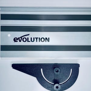 Op de afbeelding: Een zilveren en zwarte Evolution geleiderail voor een zaag met een zwarte gradenboog. Het Evolution-logo is zwart gedrukt op de geleiderail. De gradenboog heeft gradenmarkeringen en twee schroefgaten.
