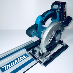 May include: A Makita cordless circular saw, featuring a silver blade and a teal and black handle. The saw is mounted on a silver and blue guide rail, with the Makita logo. A black battery pack is attached to the saw.