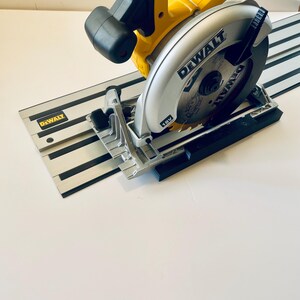 May include: A yellow and black DEWALT circular saw with a silver blade and a black guide rail. The saw is resting on a white surface. The saw blade is 18V.