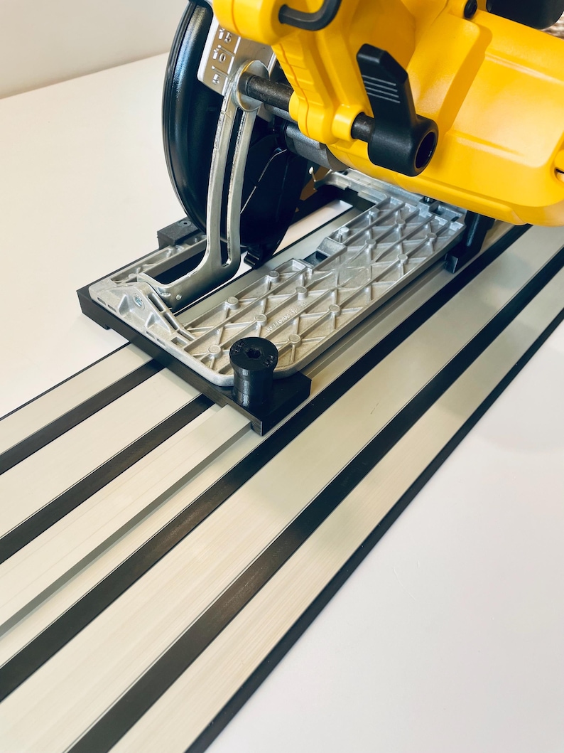 May include: A yellow and black circular saw with a silver base is positioned on a white and black track system. The saw features a black blade guard and handle. The track system has alternating white and black stripes.