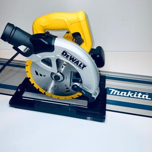 May include: A yellow and silver DeWalt circular saw with a black base and a Makita guide rail. The saw blade is yellow and silver. The saw has a black power cord.