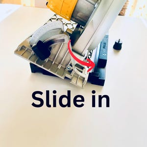 May include: A yellow and silver circular saw with a black base. The saw has a silver blade guard and a black handle. The text "Slide in" is printed on the surface. A red arrow indicates the direction of the slide.