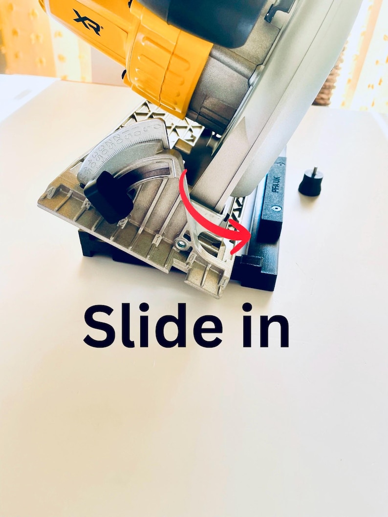 May include: A yellow and silver circular saw with a black base. The saw has a silver blade guard and a black handle. The text "Slide in" is printed on the surface. A red arrow indicates the direction of the slide.