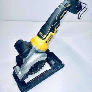 Puede incluir: Sierra circular inalámbrica con mango negro y amarillo. La sierra tiene una hoja plateada y está montada sobre una base negra. Se ve la marca "DeWALT". Diseñada para cortar madera y otros materiales.