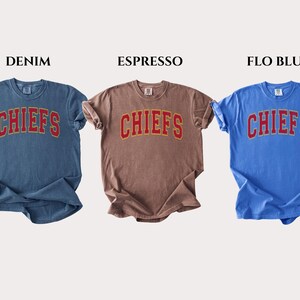 Op de afbeelding: Drie t-shirts met korte mouwen en ronde hals in denimblauw, espressobruin en flo-blauw. Elk shirt heeft het woord CHIEFS in een rood lettertype in collegestijl met een gele omlijning op de borst. De labels vermelden DENIM, ESPRESSO en FLO BLUE.