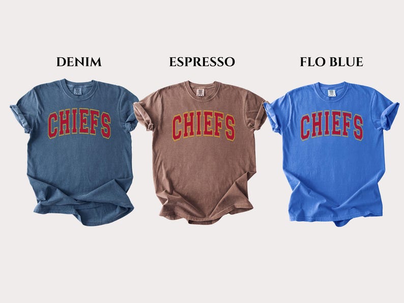 Op de afbeelding: Drie t-shirts met korte mouwen en ronde hals in denimblauw, espressobruin en flo-blauw. Elk shirt heeft het woord CHIEFS in een rood lettertype in collegestijl met een gele omlijning op de borst. De labels vermelden DENIM, ESPRESSO en FLO BLUE.
