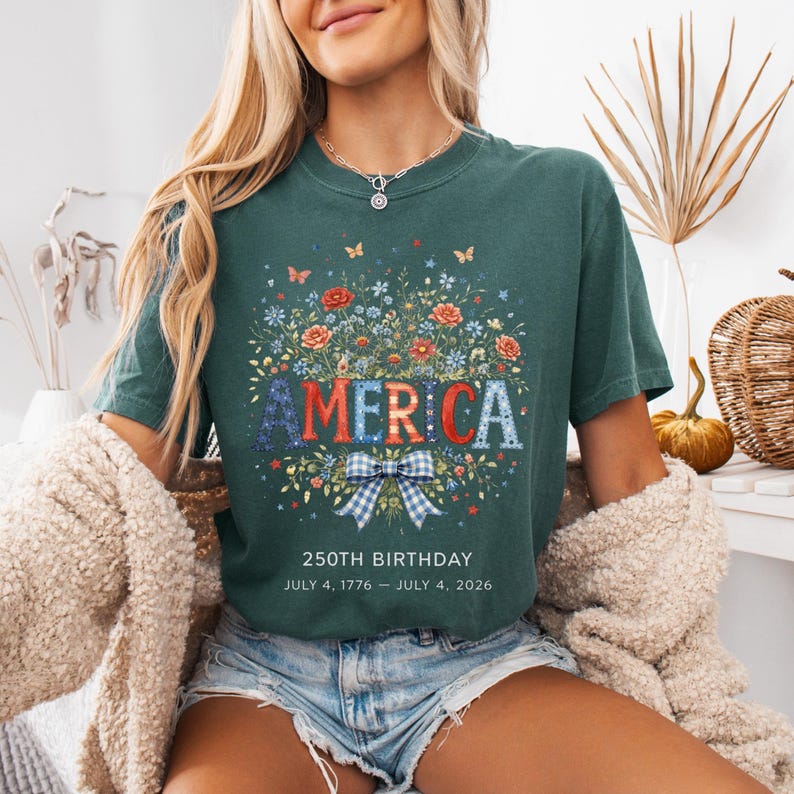 May include: Dark green t-shirt with the word "AMERICA" in red, white, and blue floral design. The shirt also features a blue and white plaid bow and the text "250TH BIRTHDAY JULY 4, 1776 - JULY 4, 2026".