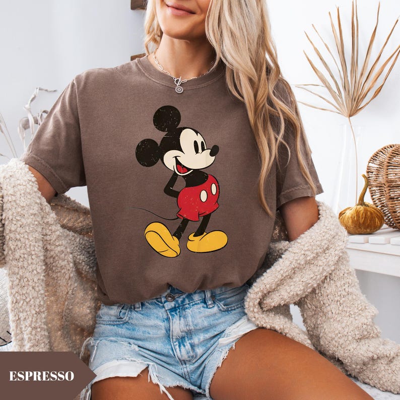 May include: Espresso-colored t-shirt featuring a classic Mickey Mouse graphic. The cartoon character is depicted in black, red, yellow, and white. The shirt is paired with denim shorts. The word "ESPRESSO" is printed at the bottom of the image.